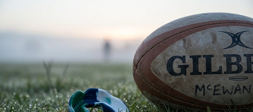 Sports mouthguard beside a rugby ball on dewy grass at dawn